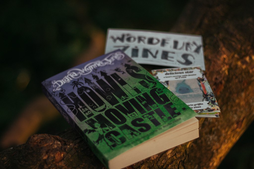 A book, a zine and a an art card lie on a thick tree branch